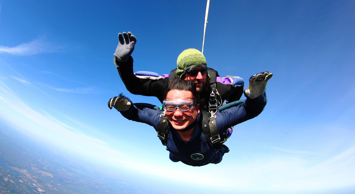 Leo Lo with diving instructor tandem skydiving under a clear blue sky.