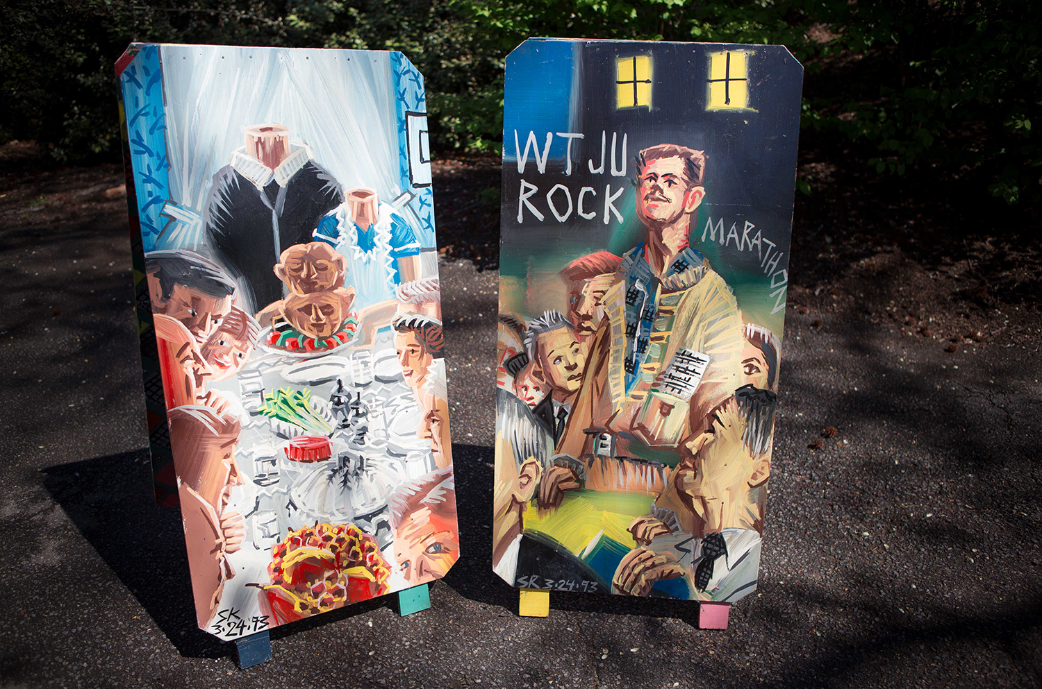 Two wooden sandwich boards with painted images: one with a headless couple serving a banquet, the other showing several men and the label WTJU Rock Marathon.