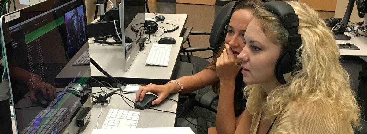 Two students in headphones work together on a desktop computer