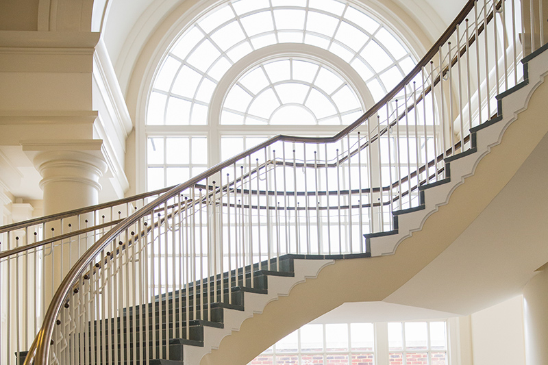 A large arched window is in front of curved circular stairs, which overlook an open space below