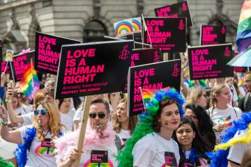 People with signs and bright clothing march in a parade. Signs read: Love is a human right