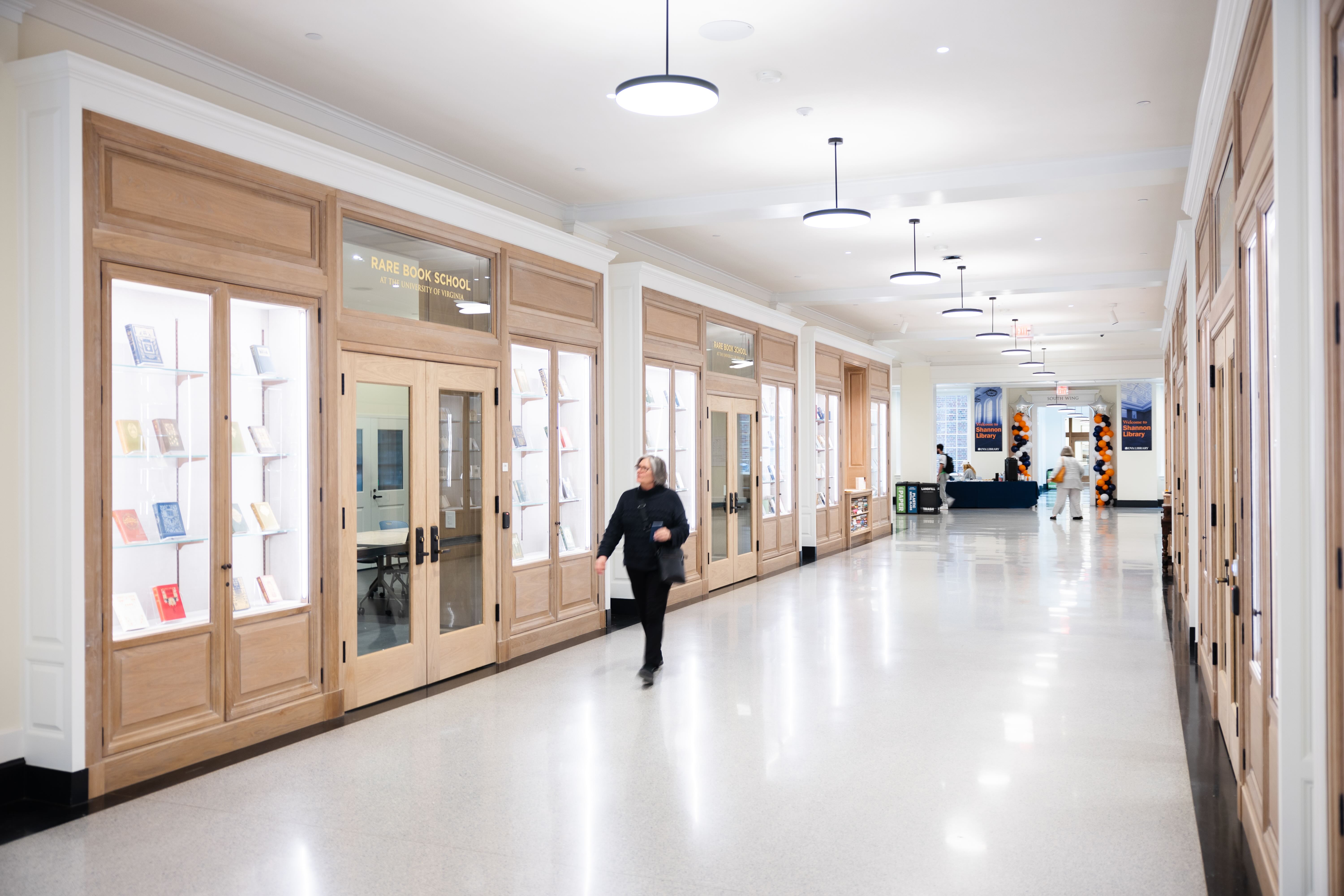 Interior of a building showing a long hallway between display cases, with a person walking and others in the background.