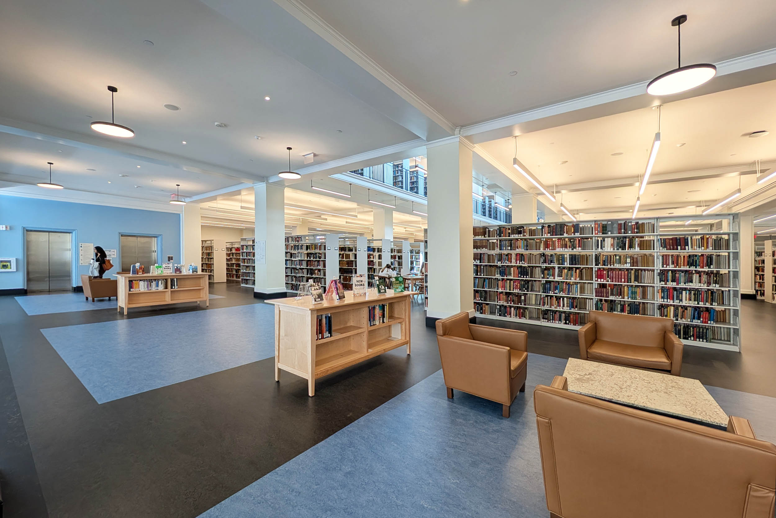 Interior of a modern library with rows of books, seating areas with couches and chairs, and bright overhead lighting.