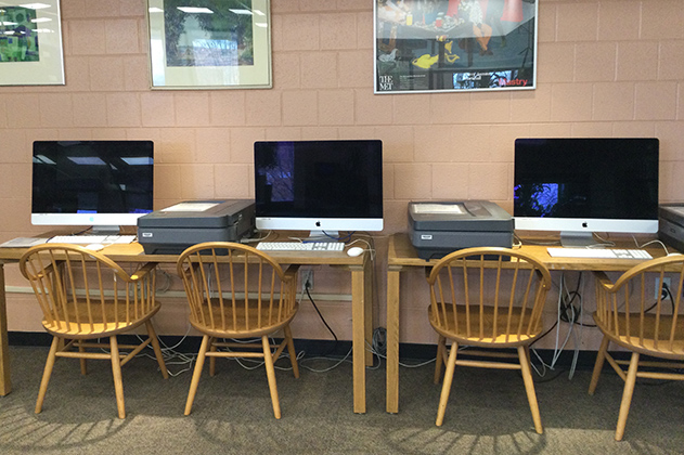 Three computers side by side, each with a wooden chair