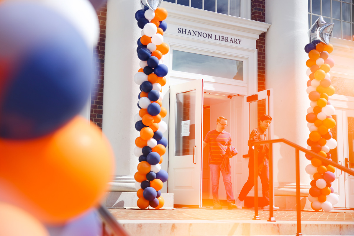 Two individuals in front of Shannon Library, which is decorated with orange and blue balloons.