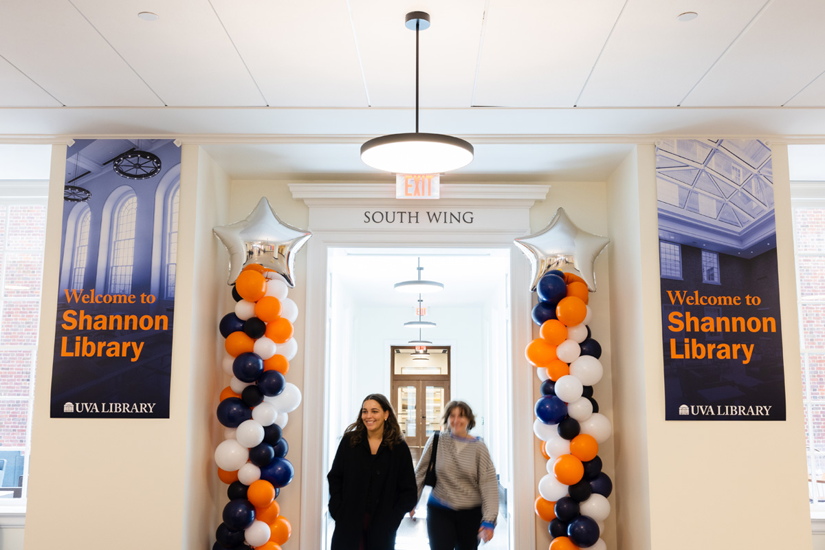 Two individuals walking out of the south wing of Shannon Library at UVA Library, through a doorway adorned with orange and blue balloons and with large banners on either side saying" Welcome to Shannon Library.