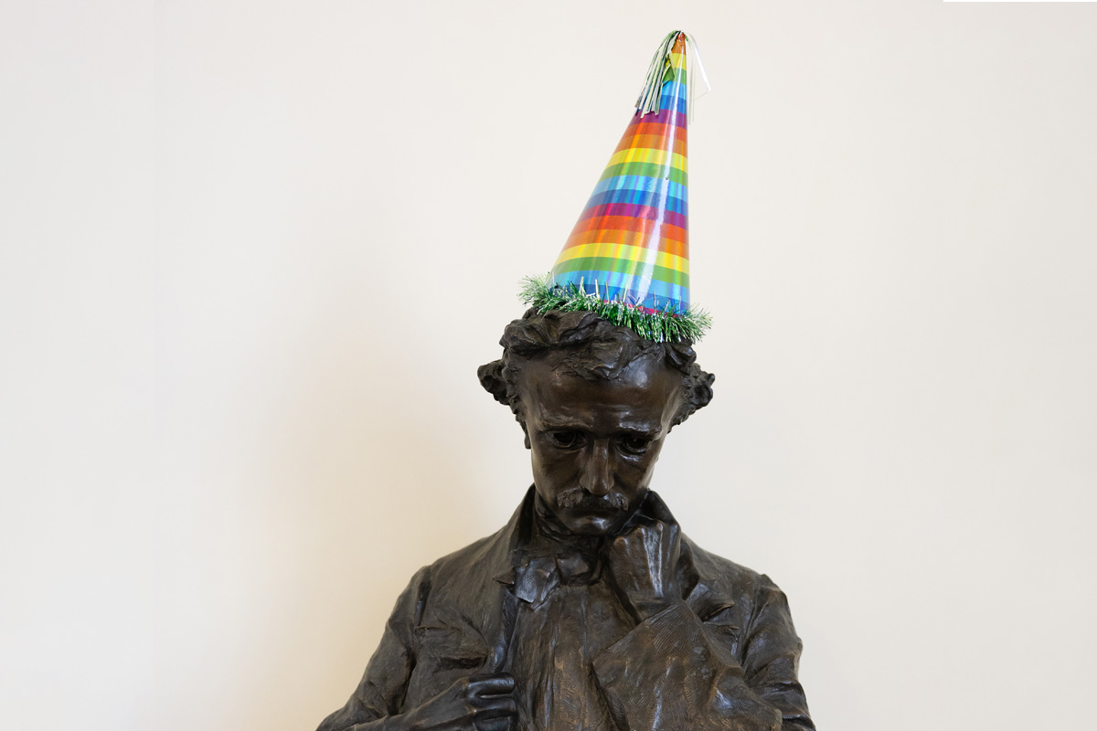 A statue of Edgar Allan Poe wearing a colorful rainbow-striped party hat.