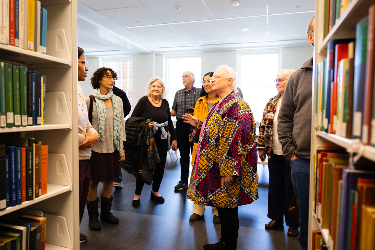 A group of adults engaging in a discussion in a library setting, surrounded by bookshelves filled with books.