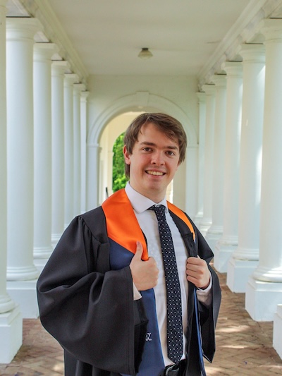A person stands in a graduation gown on the UVA campus.