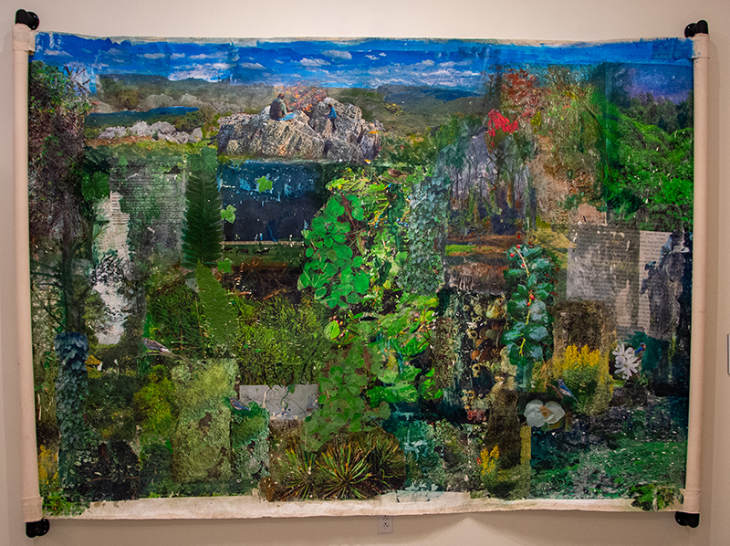 Panoramic artwork depicting a vibrant mixed-media landscape featuring various natural elements, textures, and vivid colors. Displayed in a gallery setting.