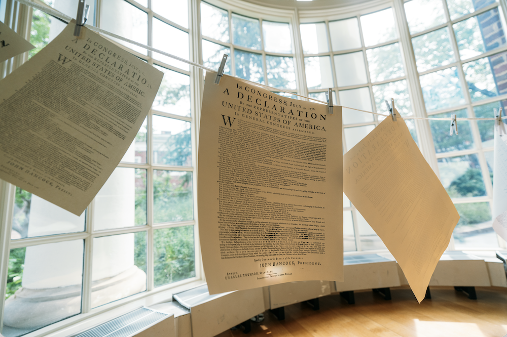Hanging replicas of the United States Declaration of Independence are displayed in front of large, curved windows, with a view of trees outside.