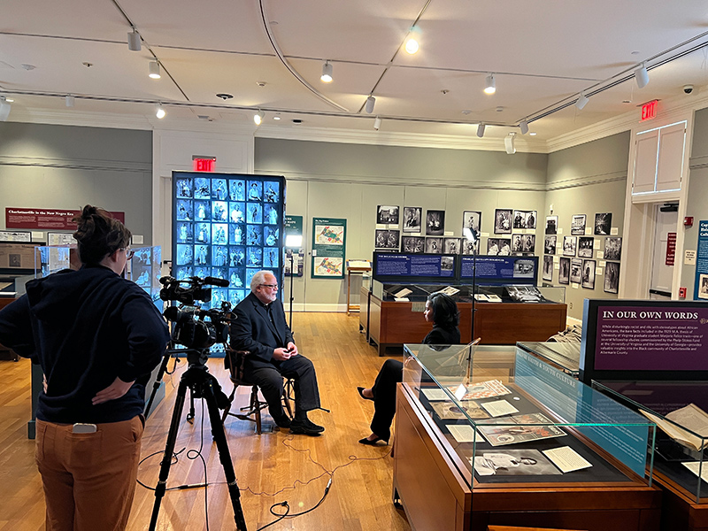 Behind-the-camera shot showing John Edwin Mason seated opposite a PBS correspondent in the exhibition room