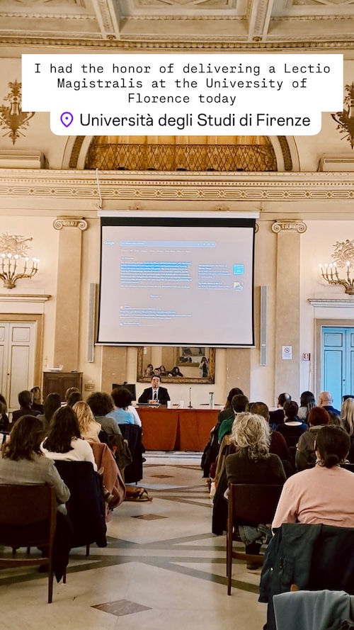 Audience seated in a large, elegant lecture hall with ornate chandeliers and decorations, listening to a presentation at the Università degli Studi di Firenze. A speaker is at a podium in front of a projection screen displaying lecture notes.