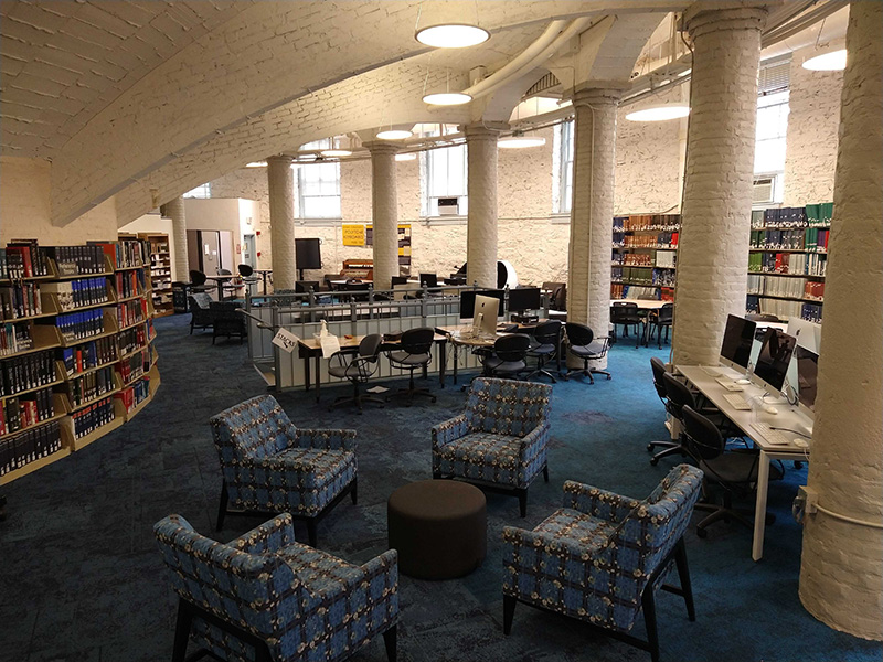 Armchairs around a small round table against a background of columns and curved walls containing shelved filled with books..