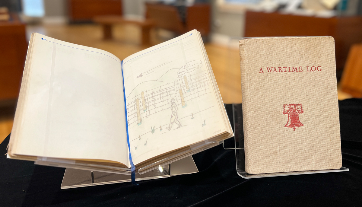 An open wartime log book with a sketch of a prison camp scene next to a second book titled 'A Wartime Log' with illustration of a red bell.