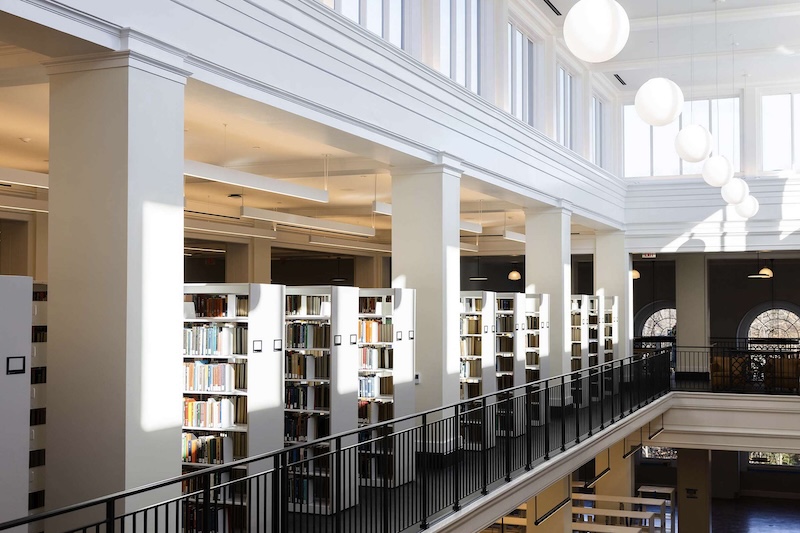 Interior of the Shannon Library, featuring neat rows of bookshelves, white columns, and large spherical white lamps hanging from the ceiling.