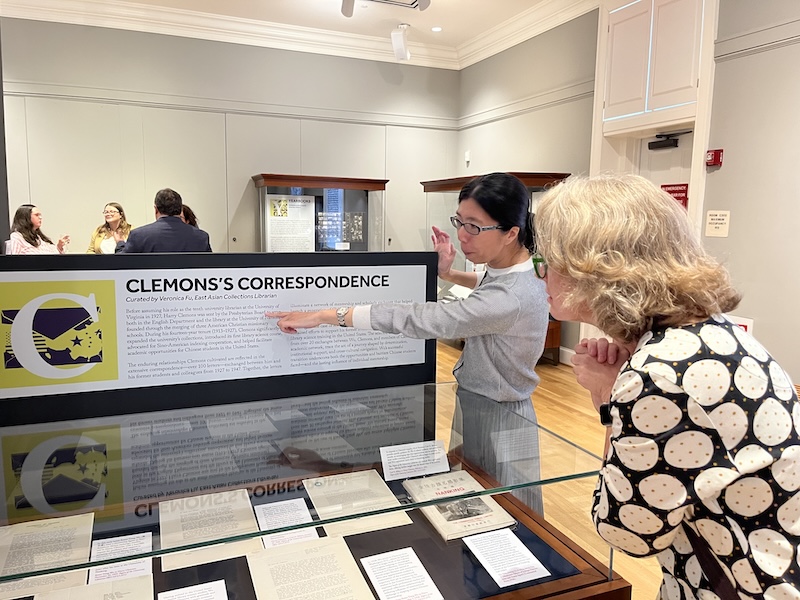Two individuals are closely examining an exhibit titled "Clemons's Correspondence" at a museum, surrounded by display cases with various documents.