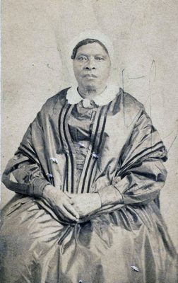 Portrait of a black woman in 19th century dress, seated, hands folded in her lap.