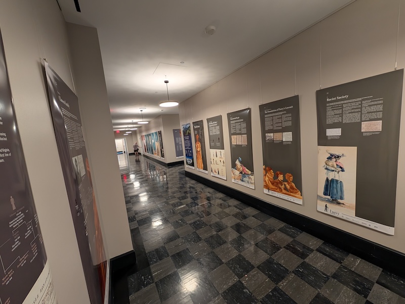 Interior of a hallway featuring an educational display with various posters and art pieces on the walls. The floor is tiled, and there are ceiling lights illuminating the space.