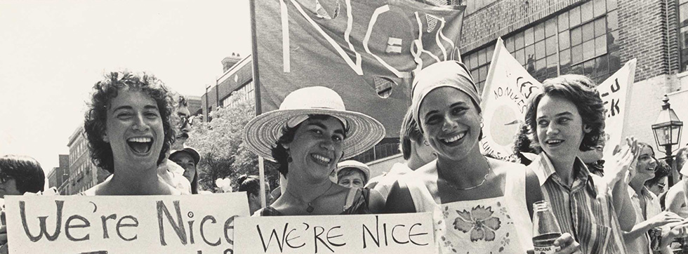 Women marching, laughing and smiling, carrying banners that read "We're nice."