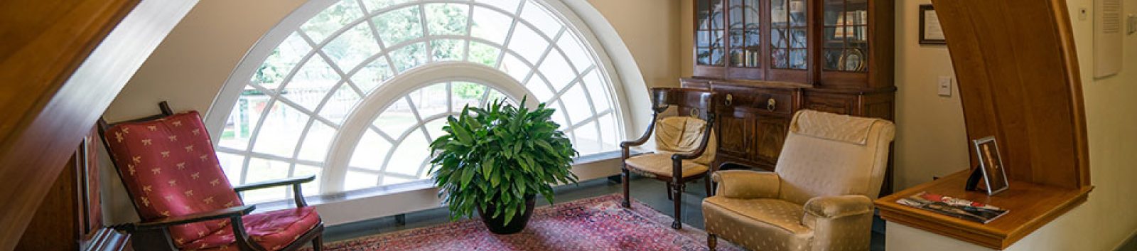 A small carpeted room with comfortable seating and a large arched window