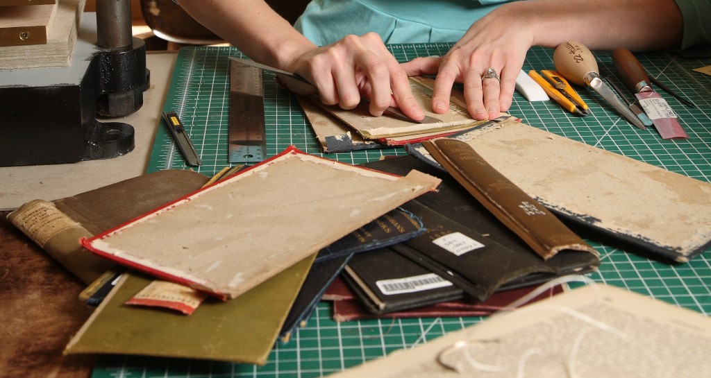 A preservationist cuts apart book bindings with a knife