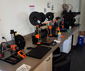 A row of 3D printers on a counter top. There is a drawing of an octopus nearby