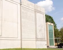 A concrete building with glass addition surrounded by green grass and trees
