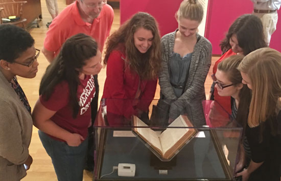 A group of women gathered around a display case containing a rare open book.