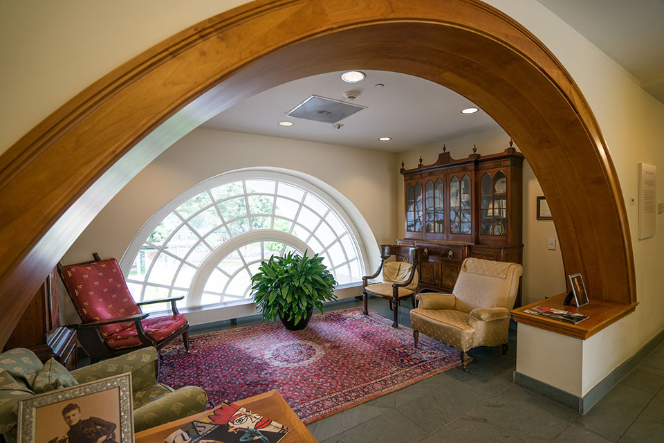 A carpeted sitting room under an archway, with windows and streaming sunlight.